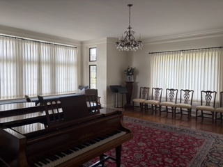 The Deanery's living room with a grand piano, chandelier, and a row of chairs set along the wall